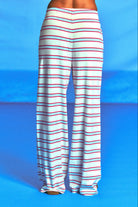 White wide-leg pants with thin red and blue horizontal stripes, shown from the back on a model against a bright blue studio background.